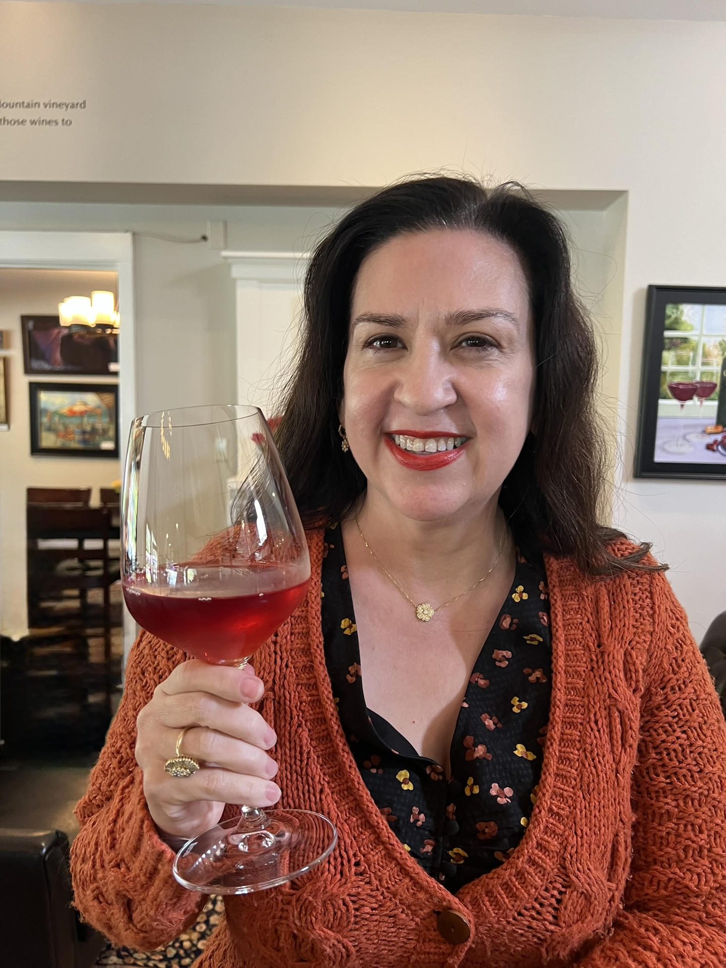 Woman smiling, holding a glass of rosé wine indoors.