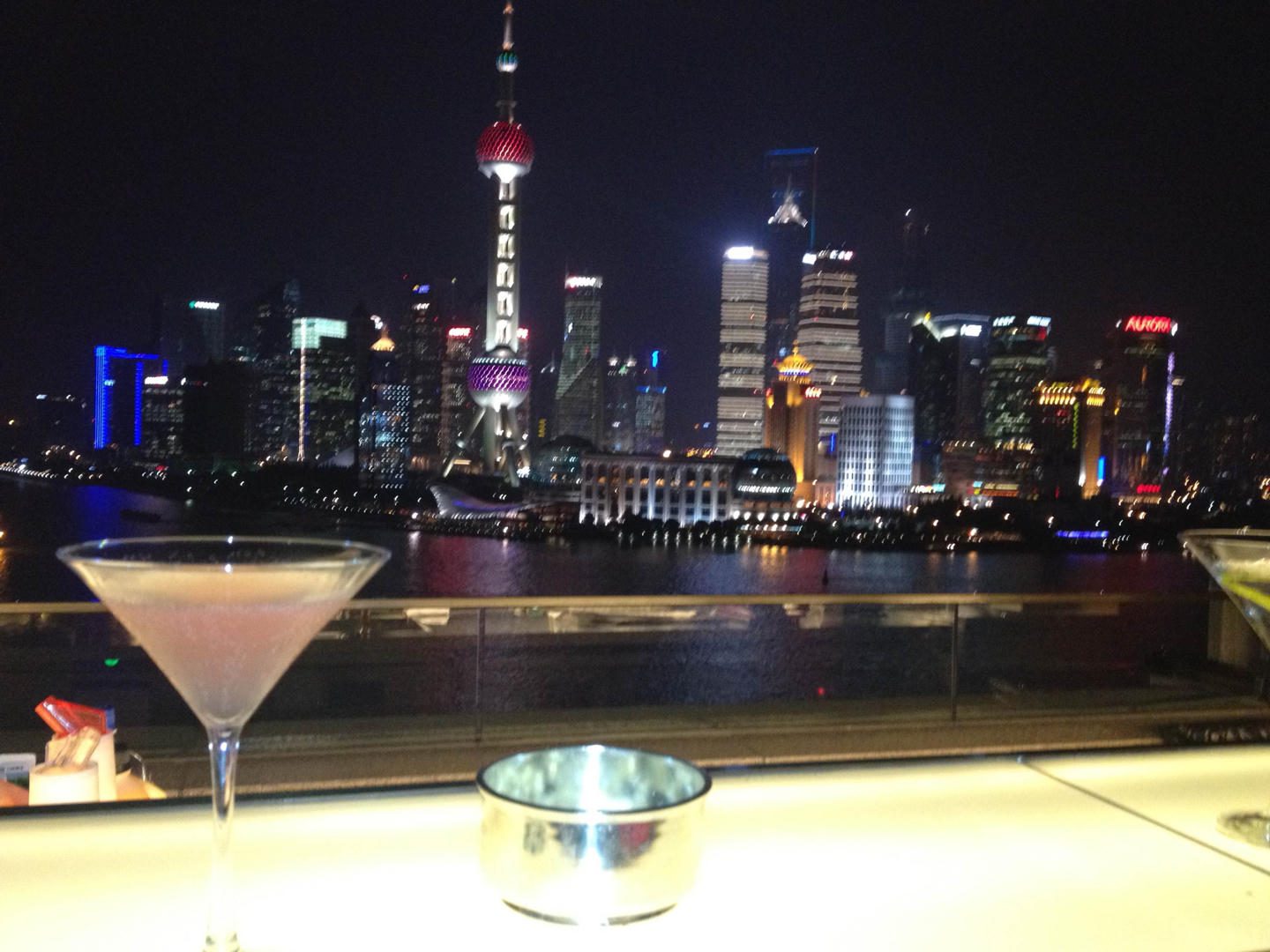 Cocktail glass and ashtray with illuminated city skyline at night.