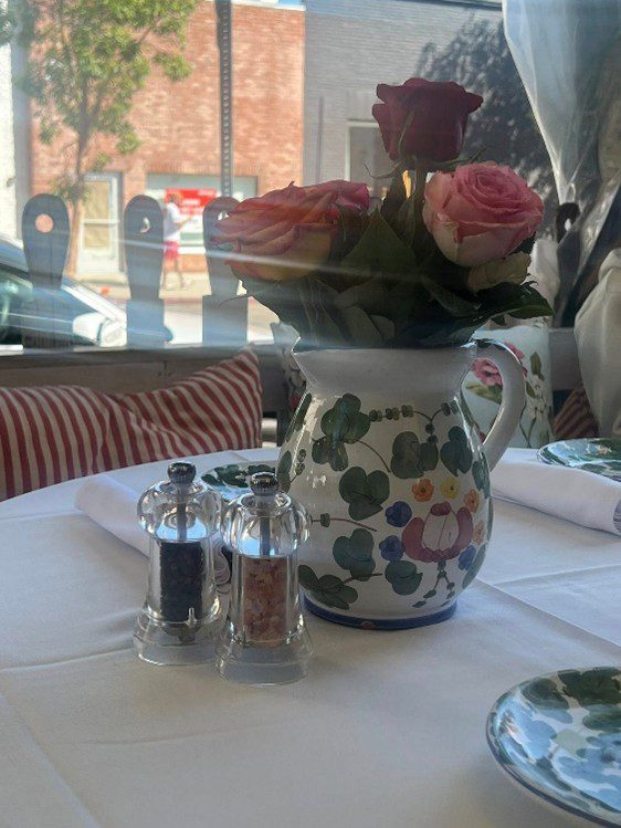 Floral pitcher holding pink roses on a dining table with salt and pepper shakers.