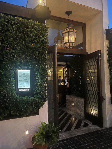 Entrance of a warmly lit restaurant with greenery and a menu display.