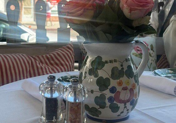 Floral pitcher holding pink roses on a dining table with salt and pepper shakers.