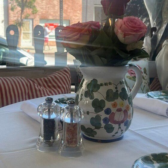 Floral pitcher holding pink roses on a dining table with salt and pepper shakers.