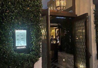 Entrance of a warmly lit restaurant with greenery and a menu display.