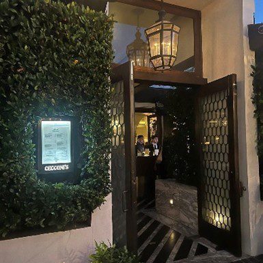Entrance of a warmly lit restaurant with greenery and a menu display.